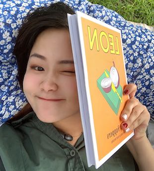 Image shows illustration student Xuan Liu lying on a picnic blanket and partially obscuring her face with a book